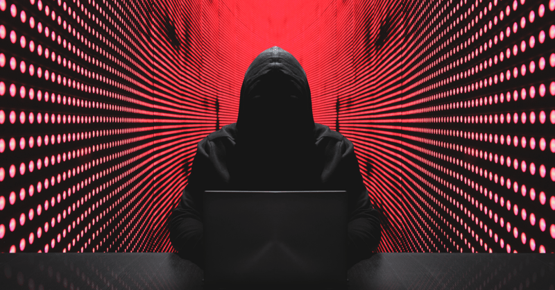 Image shows a cyber hacker's silhouette, with a red background behind them
